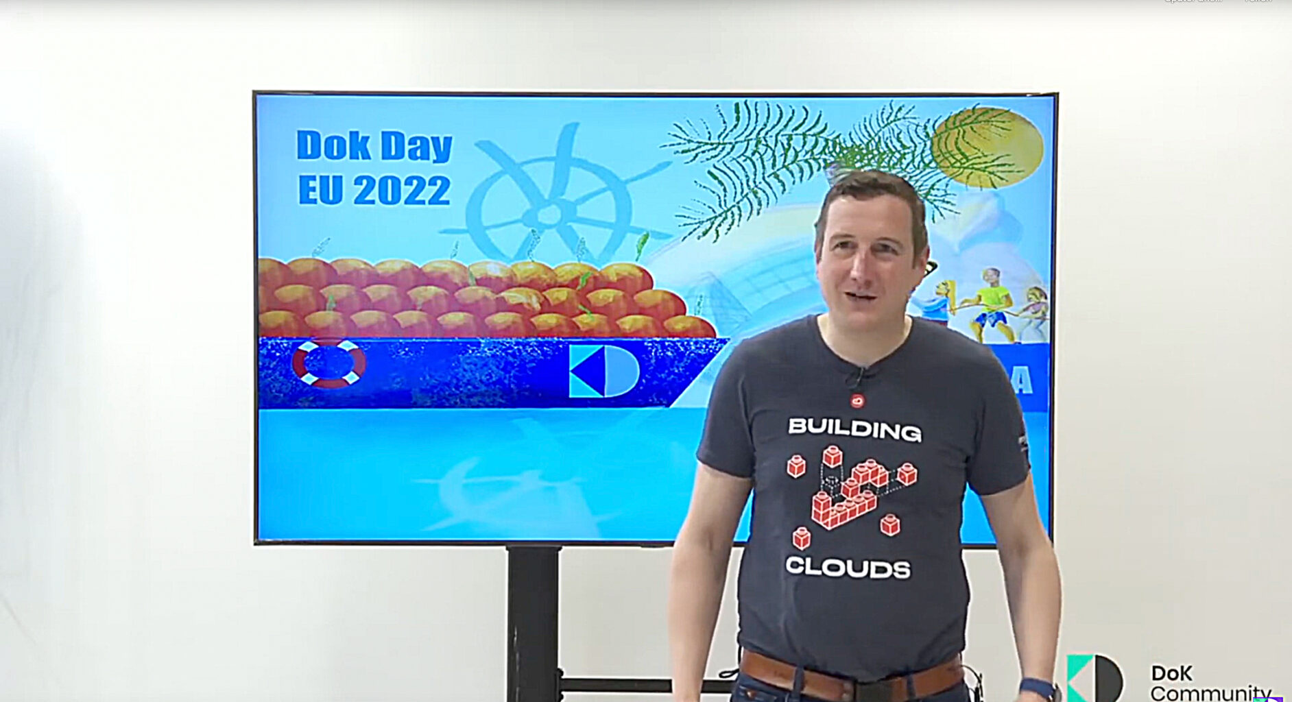 A man stands in front of a TV displaying a video game, focused on the action on the screen. While wearing a shirt from anynines - Building Clouds.
