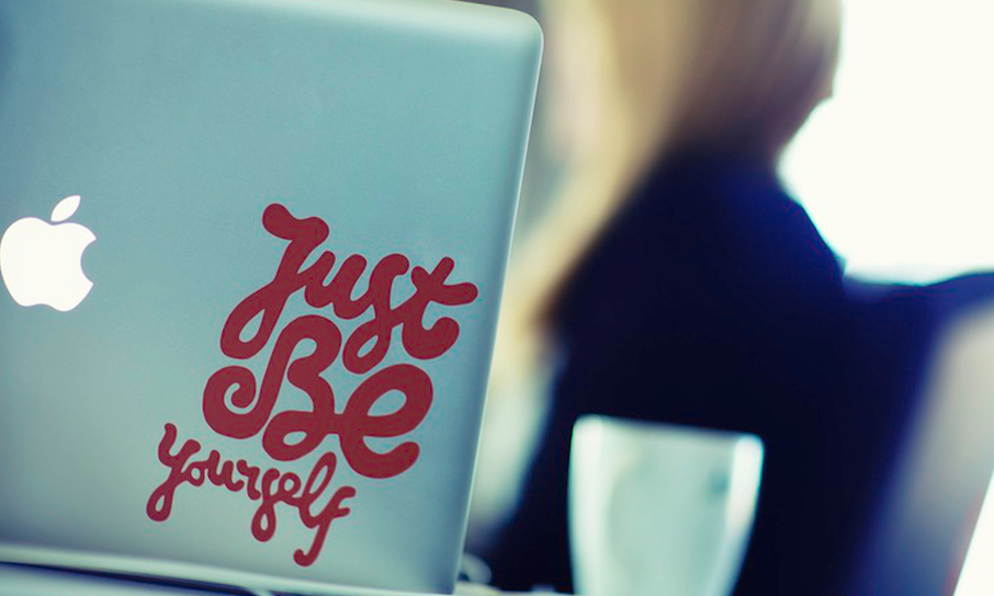 We see an office table, with a coffee mug, an apple laptop, and a sticker.