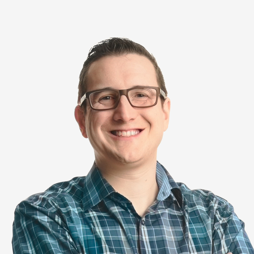 a man smiling in the foreground, wearing glasses and a green shirt.