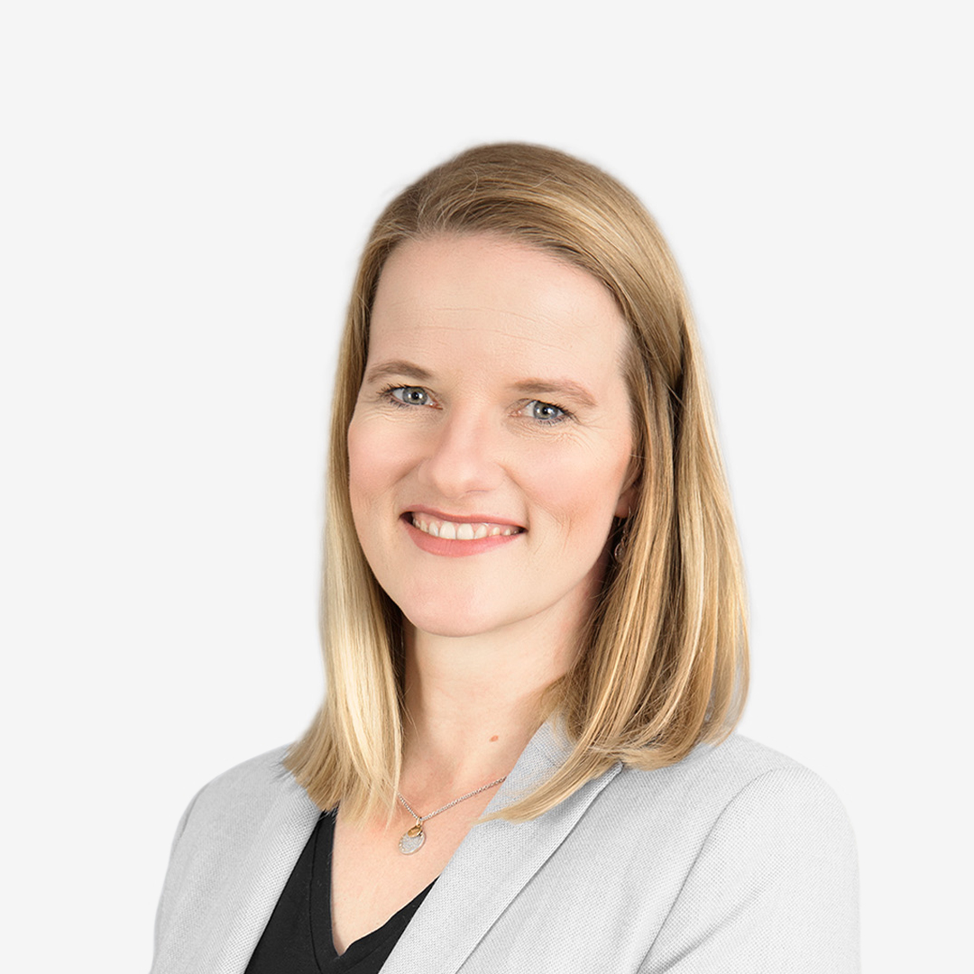 A women smiling in the foreground, wearing a grey jacket.